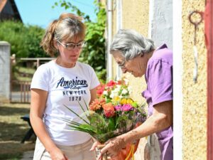 A woman gifts a vibrant bouquet to an elder outside a French house.